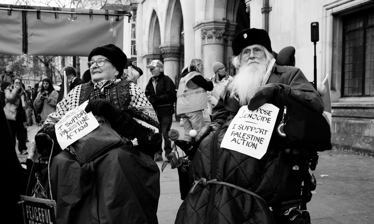 Two demonstrators in wheelchairs wearing 'I Support Palestine Action' signs outside the Royal Courts of Justice, London